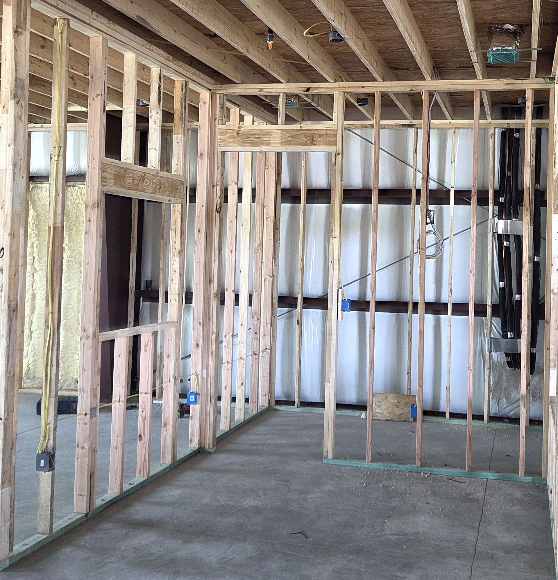 Interior of a room under construction with wooden framing, visible studs, and concrete floor.