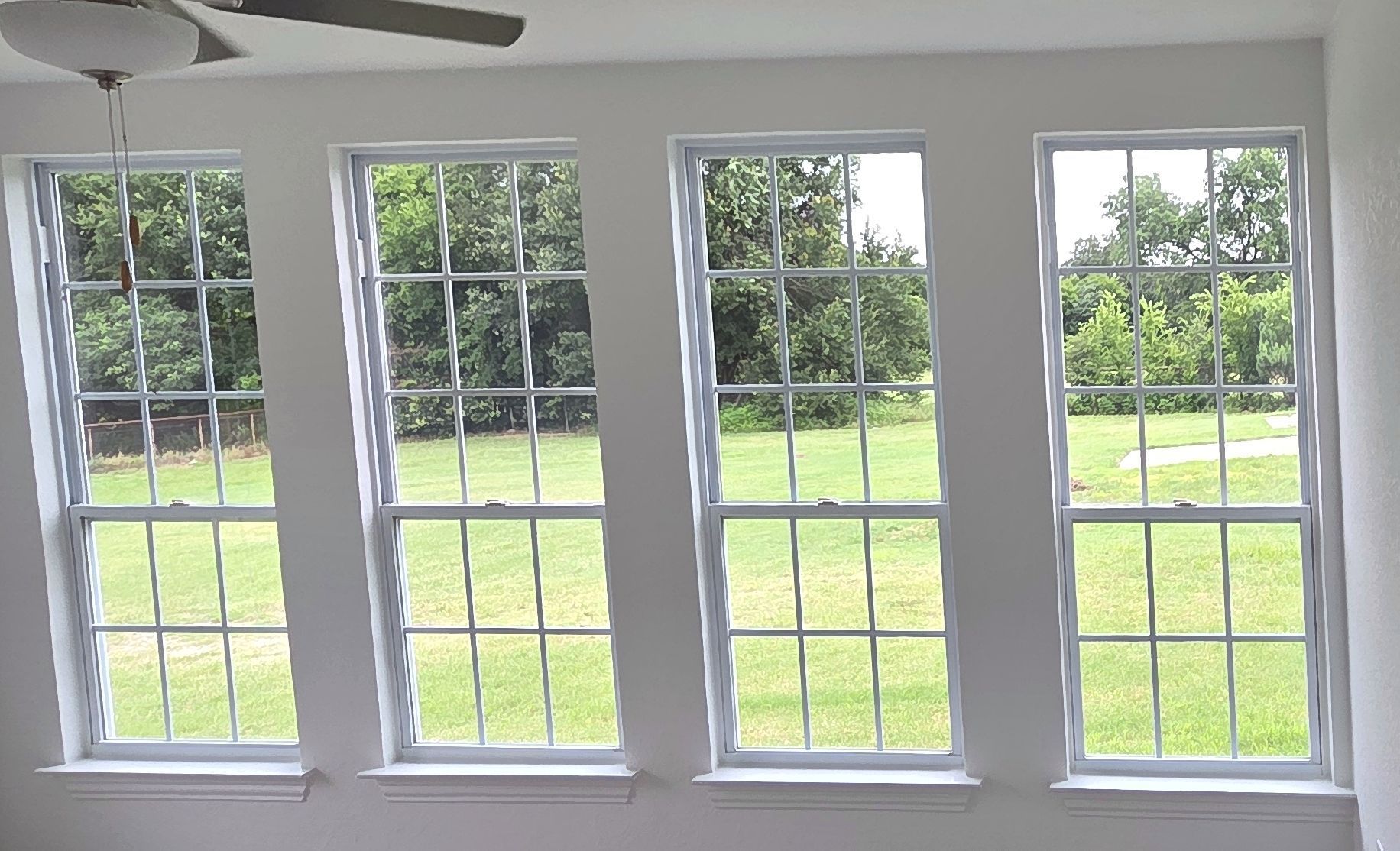Four white-framed windows with grid patterns, angled slightly, overlooking a grassy yard with trees.