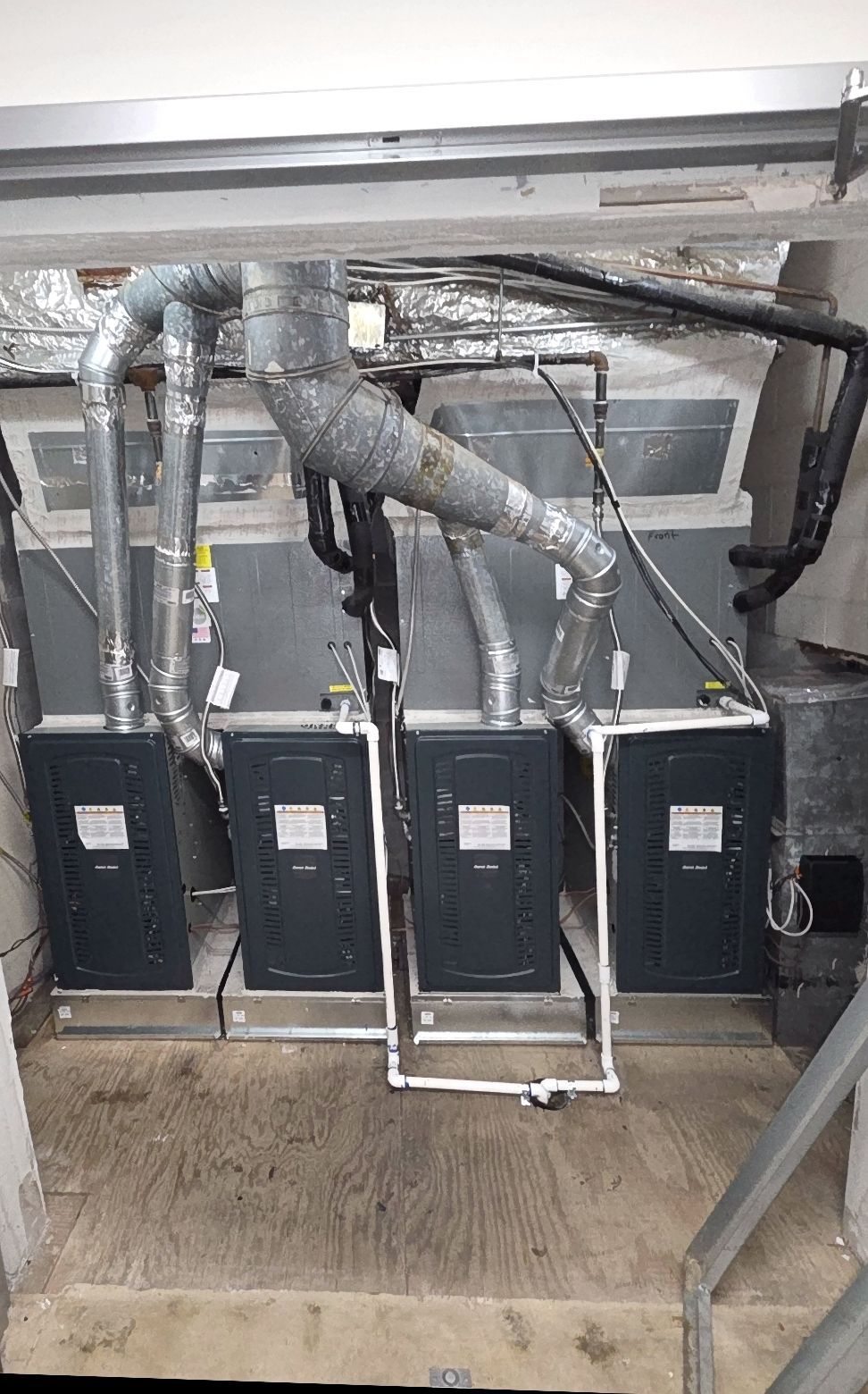 Three dark-colored HVAC units installed in a row inside an enclosed space, with silver ductwork.