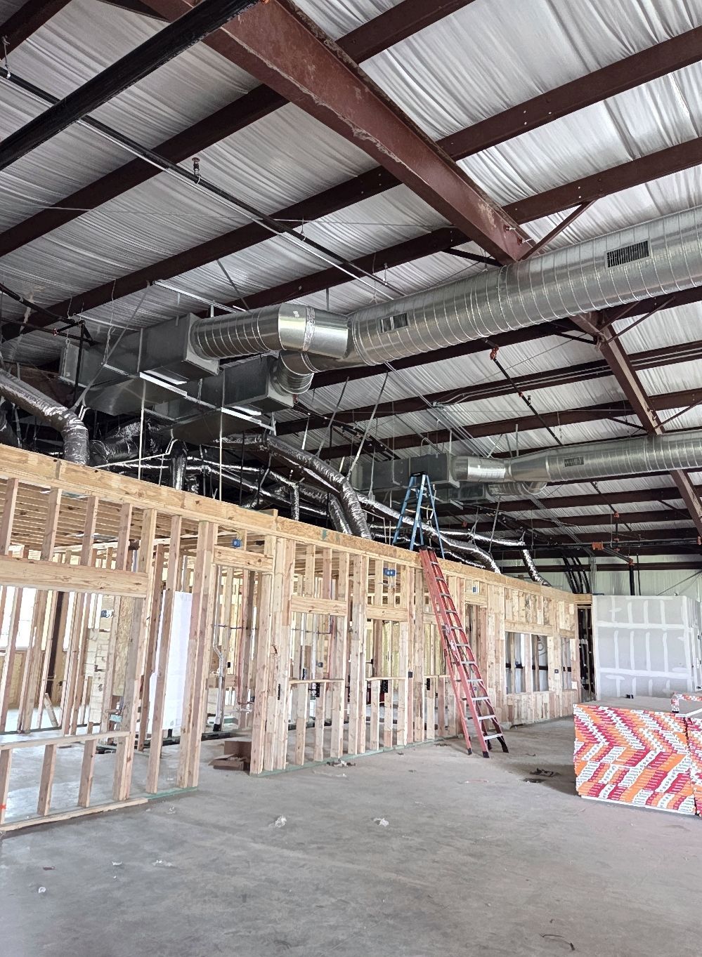Interior of a building under construction. Wooden framing for walls is visible, with exposed ductwork and metal beams overhead.