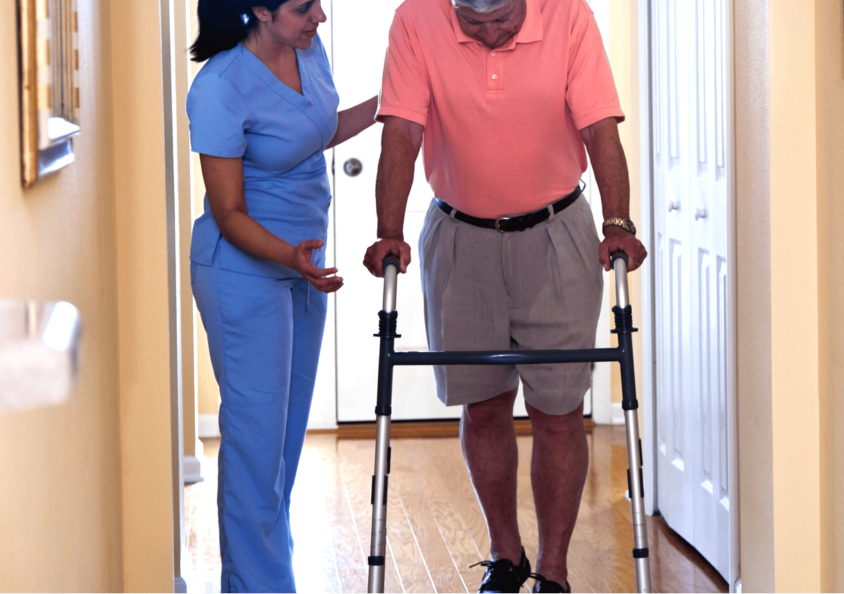 A nurse helps an elderly man walk with a walker