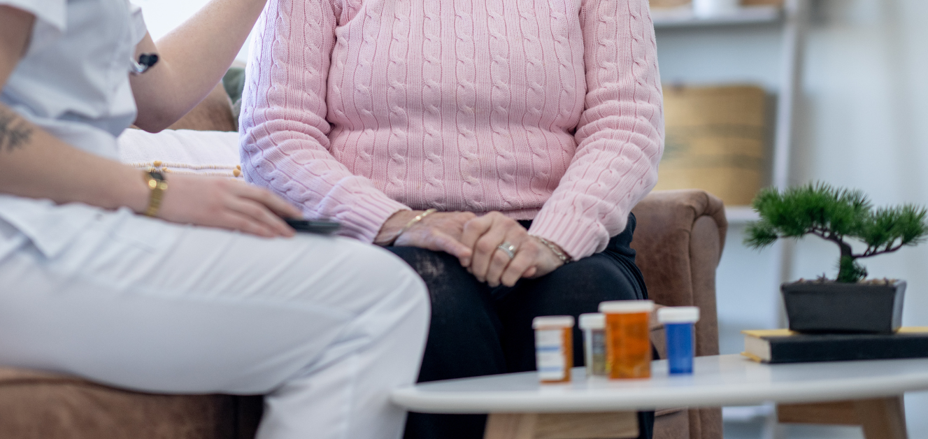 An elderly woman is sitting on a couch with a nurse.