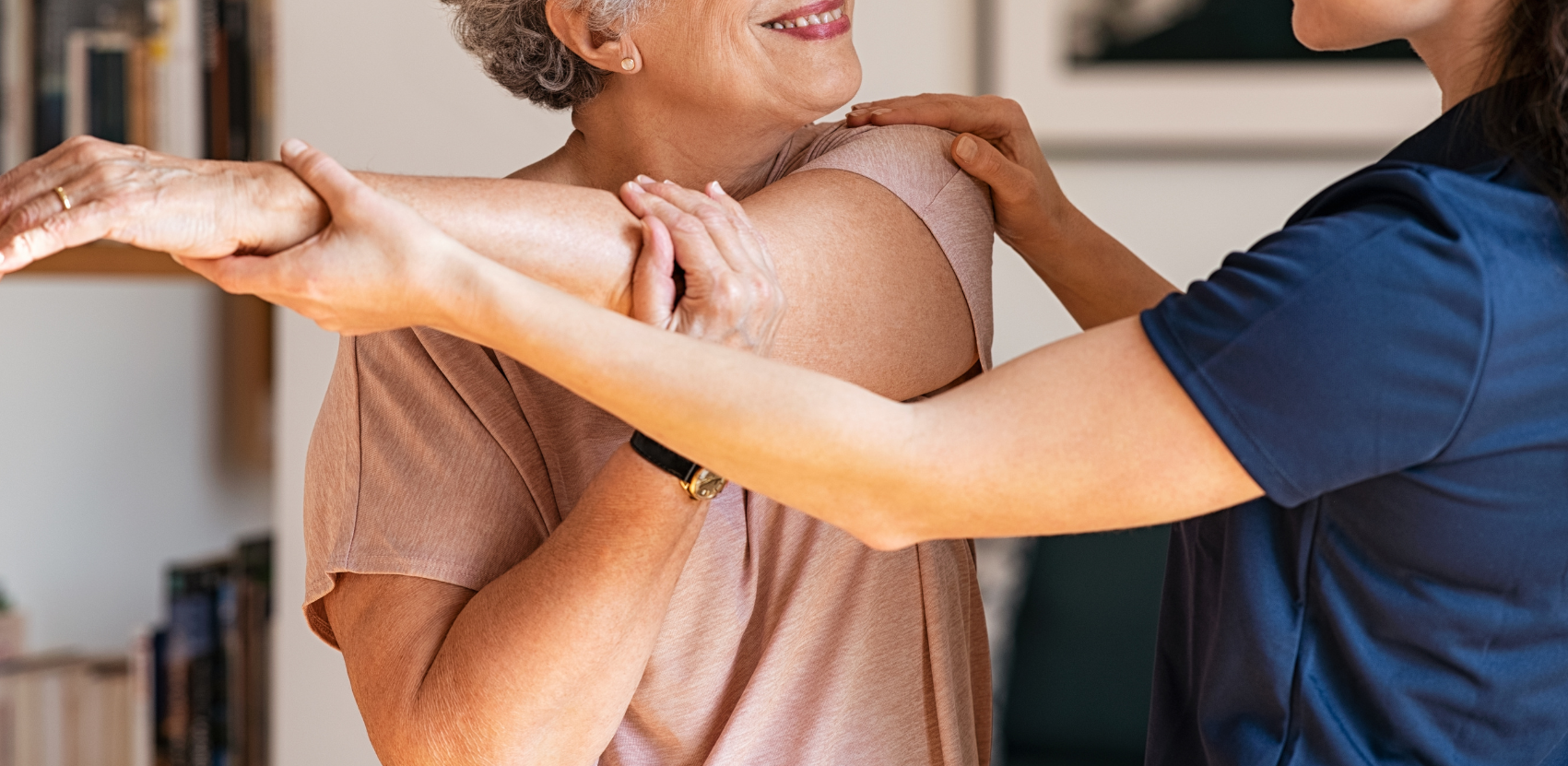 An elderly woman is being helped by a nurse to stretch her arms.