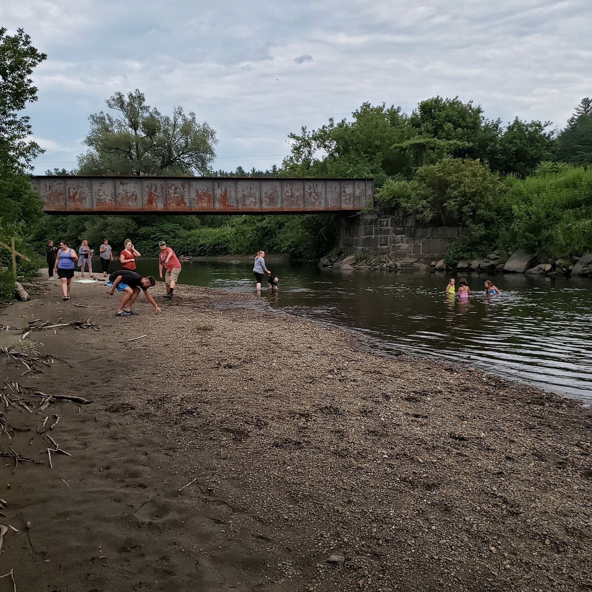 A group of people are playing in the water under a bridge.