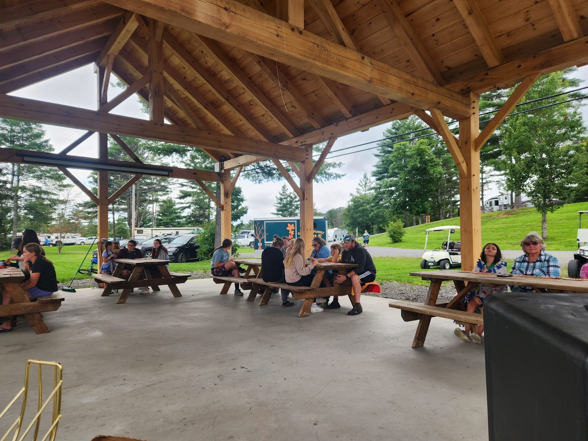 A group of people are sitting at picnic tables under a wooden roof playing games