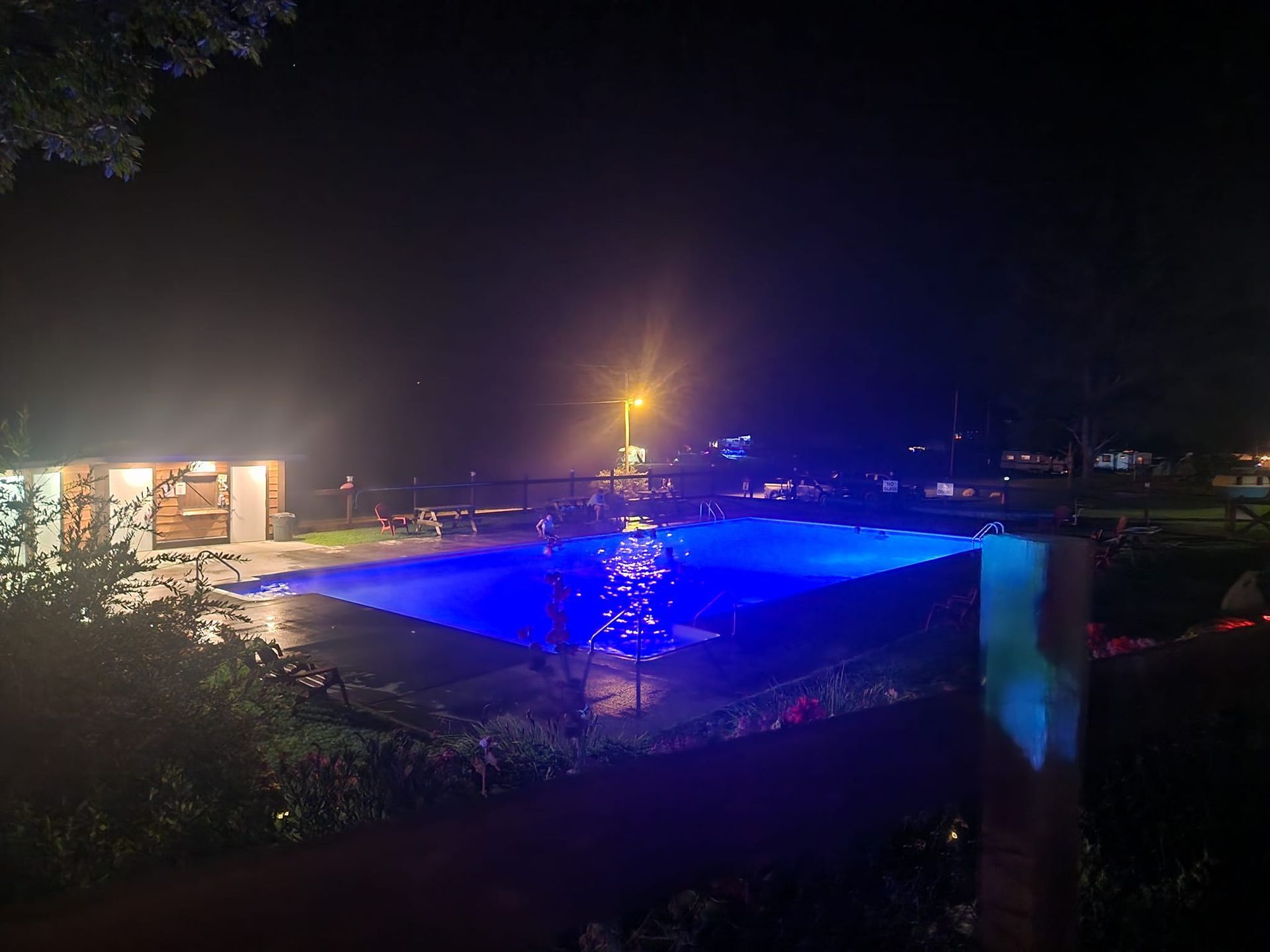 A large heated salt water swimming pool is lit up at night with blue lights.