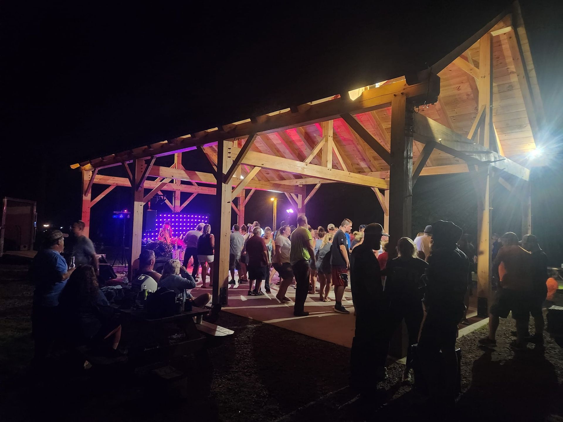 A group of people are dancing under the pavilion at night.