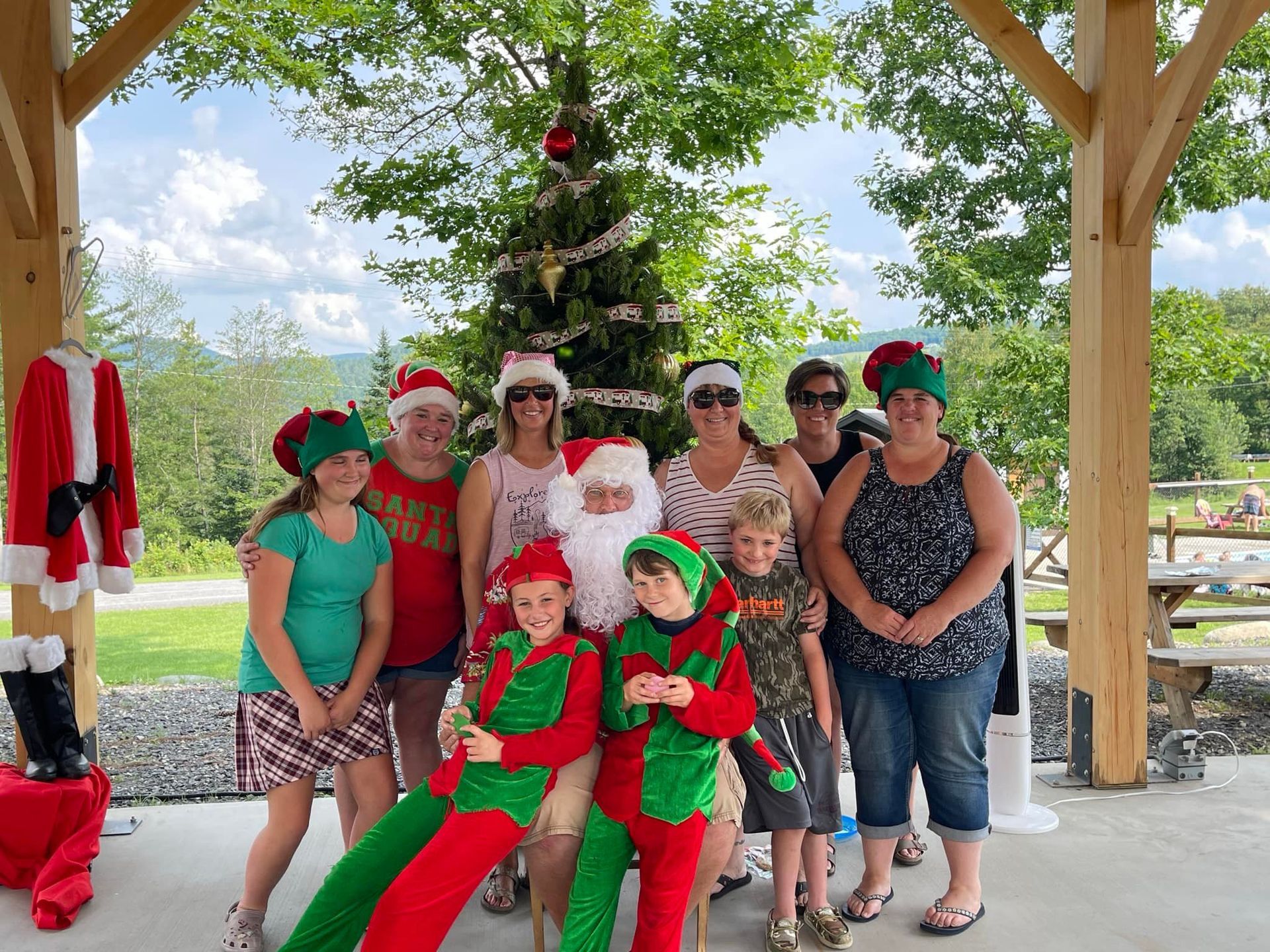 A group of people are posing for a picture with Santa Claus and elves in front of a Christmas tree.