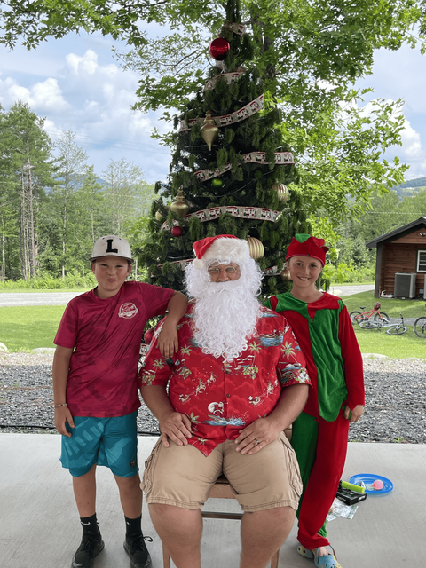 A man dressed as Santa Claus is sitting next to two children in front of a Christmas tree.