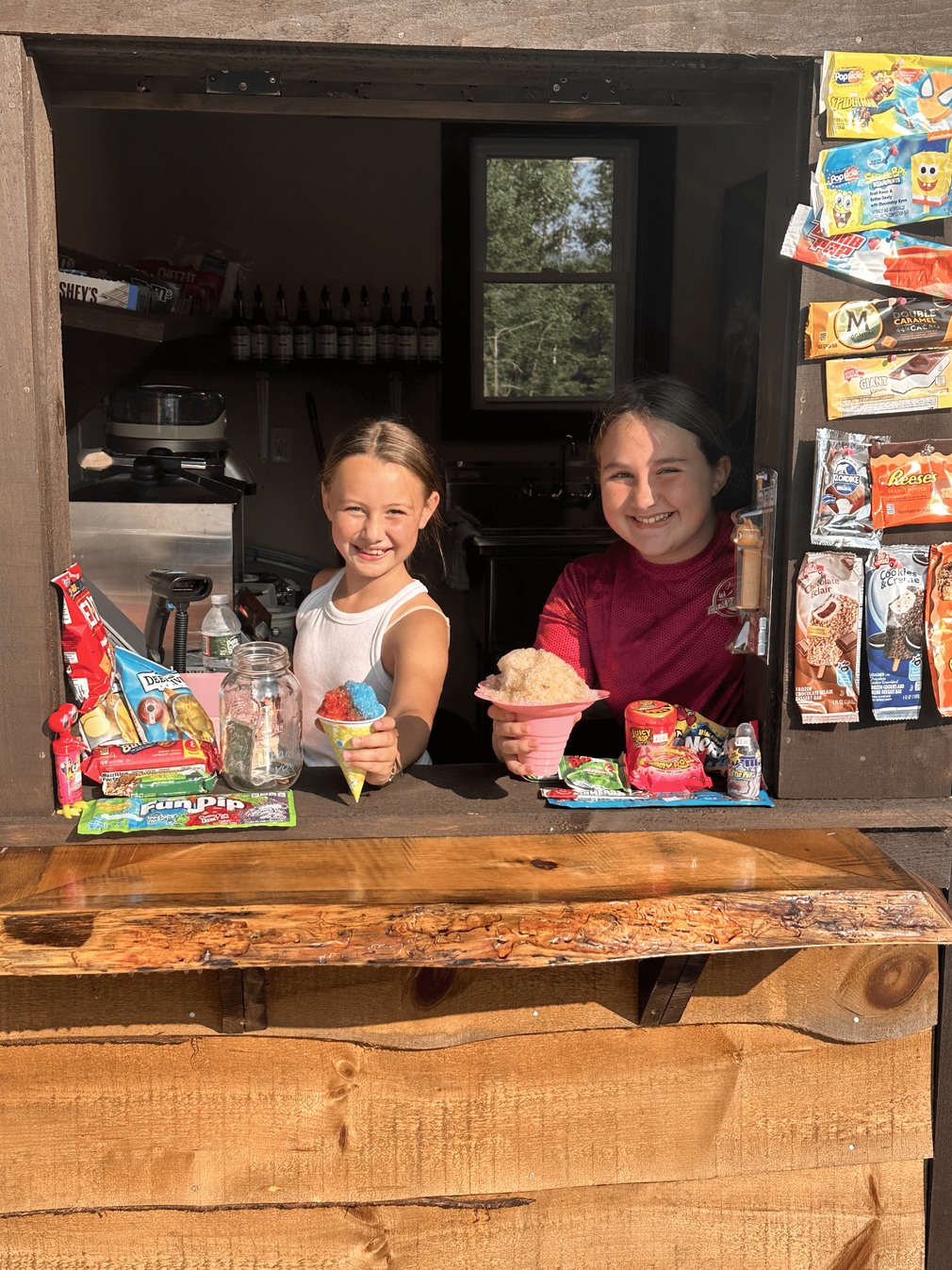 Two young girls are standing behind a counter holding ice cream cones.