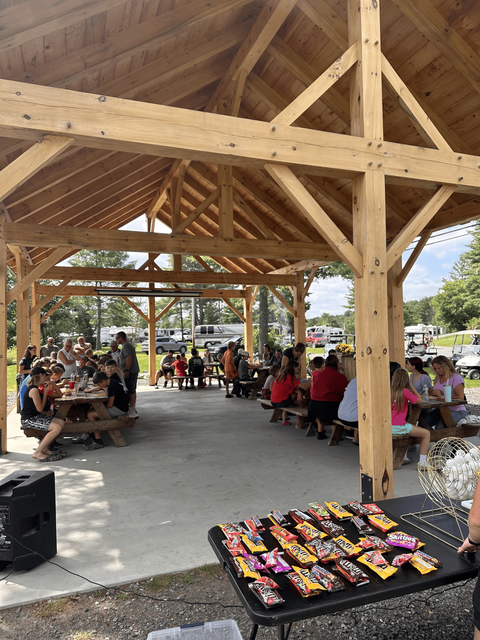 A group of people are sitting at picnic tables under a wooden pavilion playing games