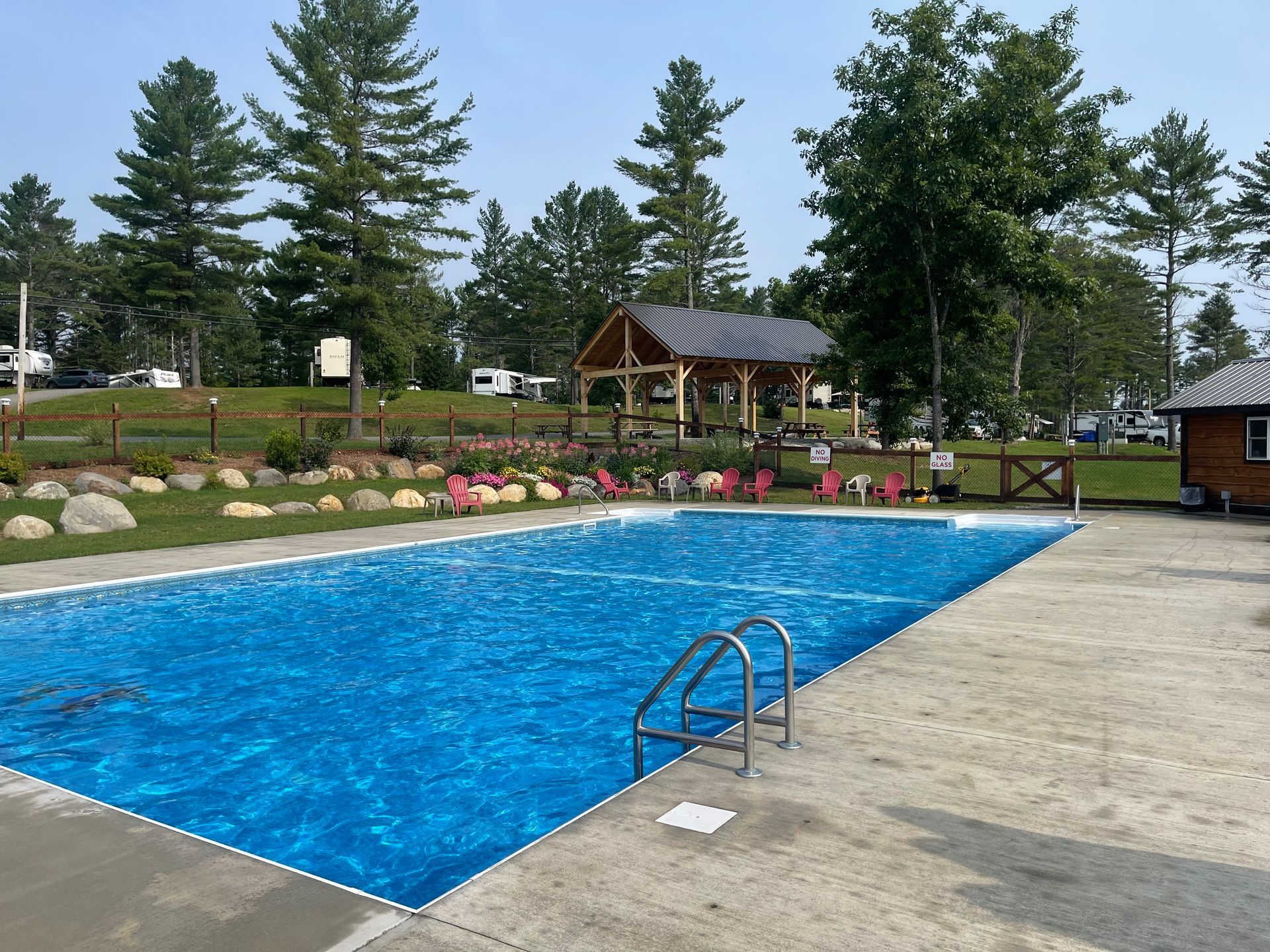 A large heated salt water swimming pool is surrounded by trees and a gazebo.