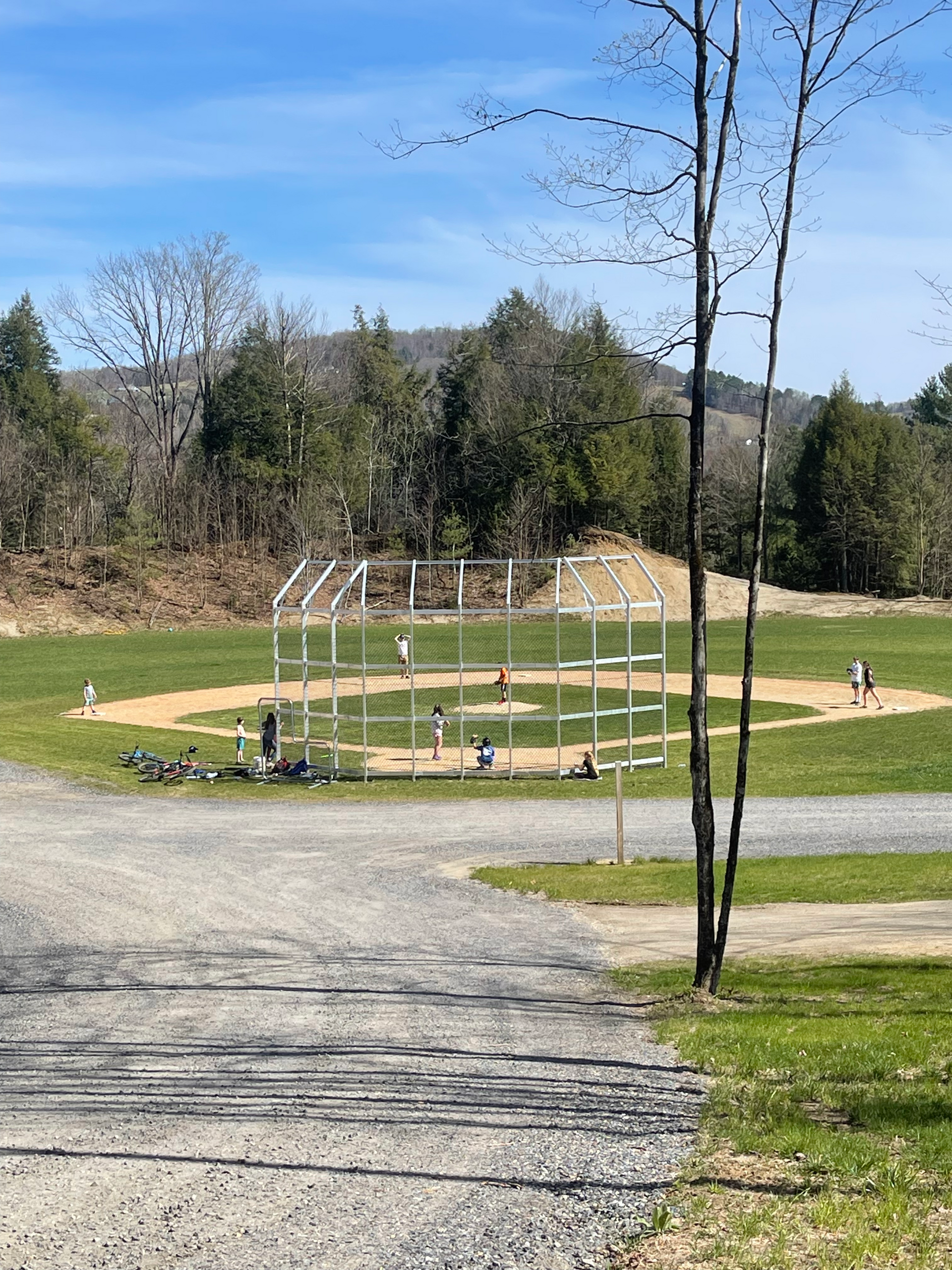 A baseball field is surrounded by trees and a gravel road.
