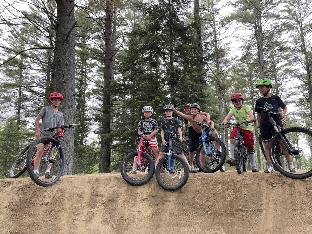 A group of young boys are posing for a picture with their bikes on a dirt track.