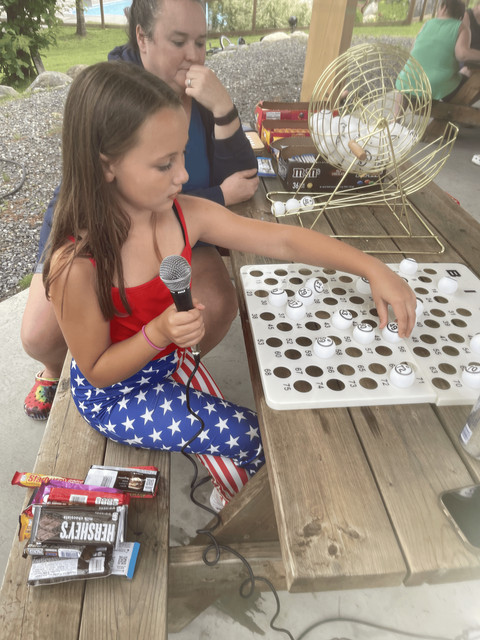 A little girl is sitting at a picnic table playing bingo