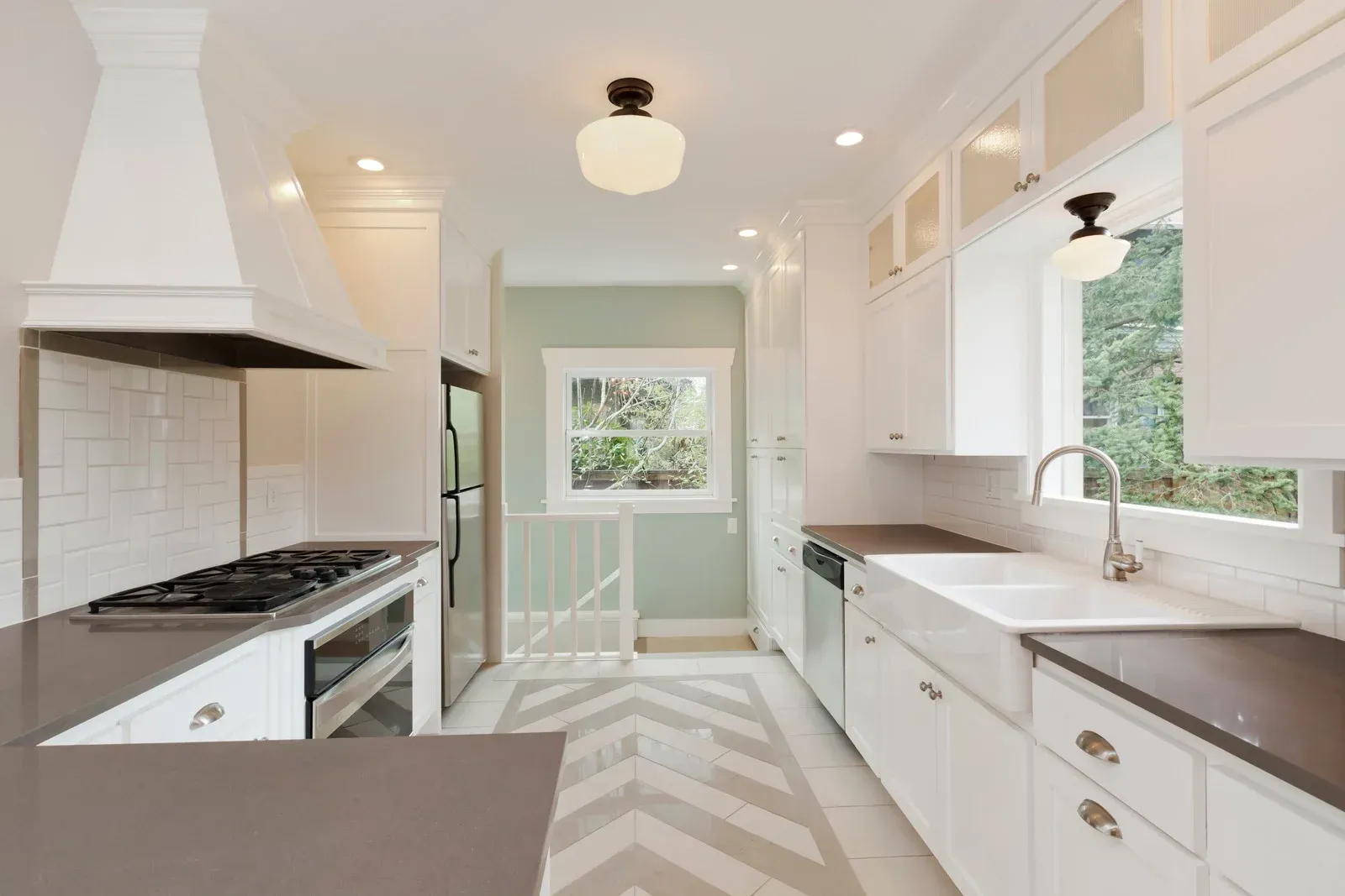 White kitchen with dark countertops, stove, and chevron patterned tile floor.