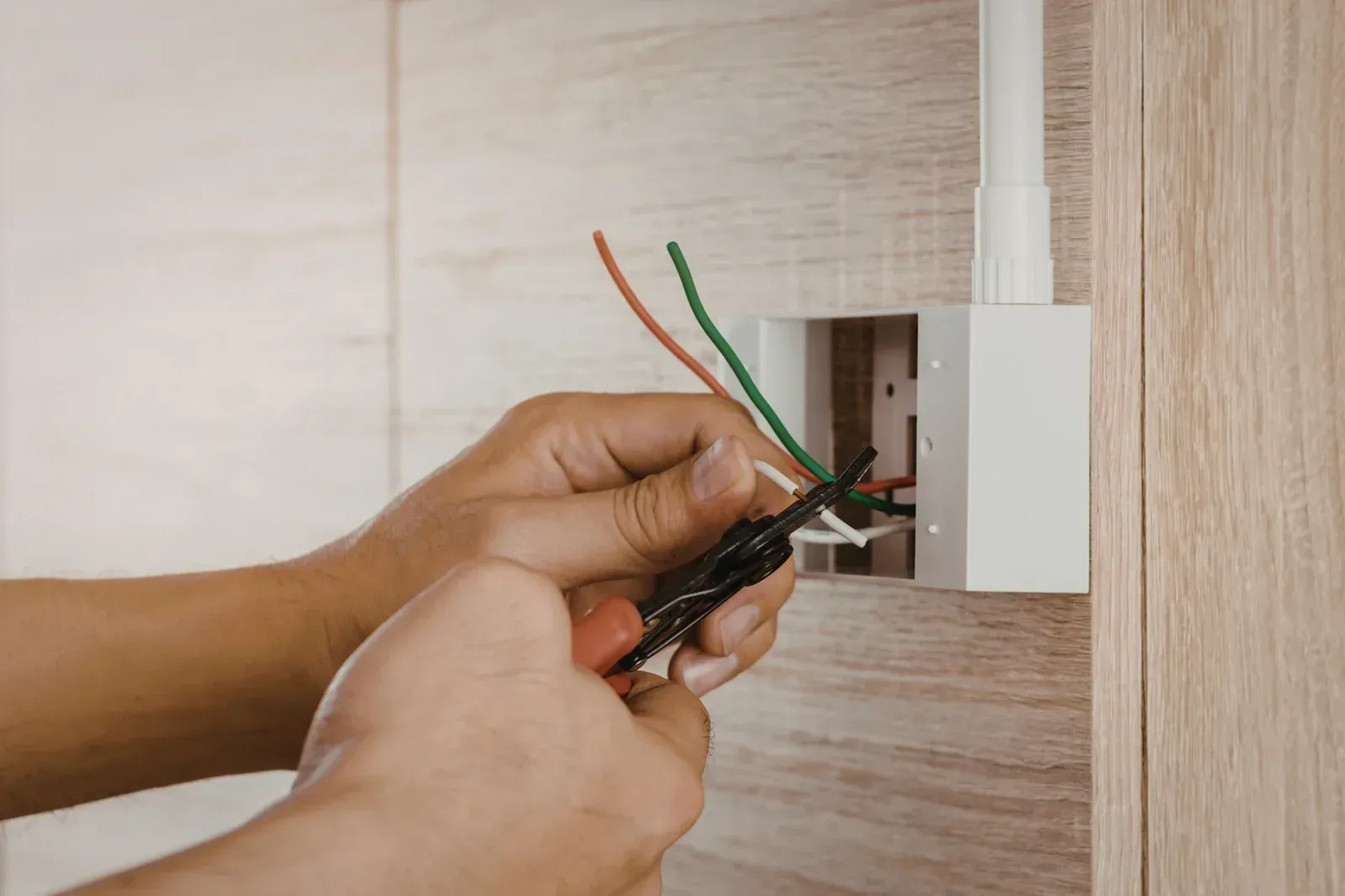 Electrician using a multimeter to test wiring inside an electrical panel.