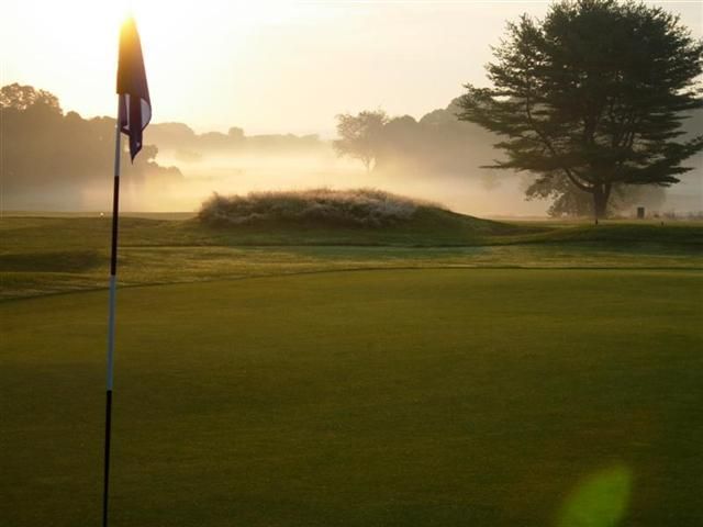 Golf course at sunrise with a flagstick, mist, and trees in the background