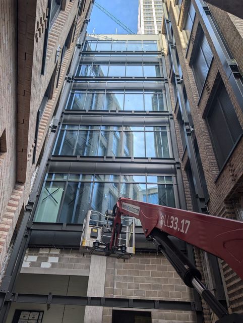 A worker assembles a glass railing with a metal handrail in a modern, under-construction interior space.