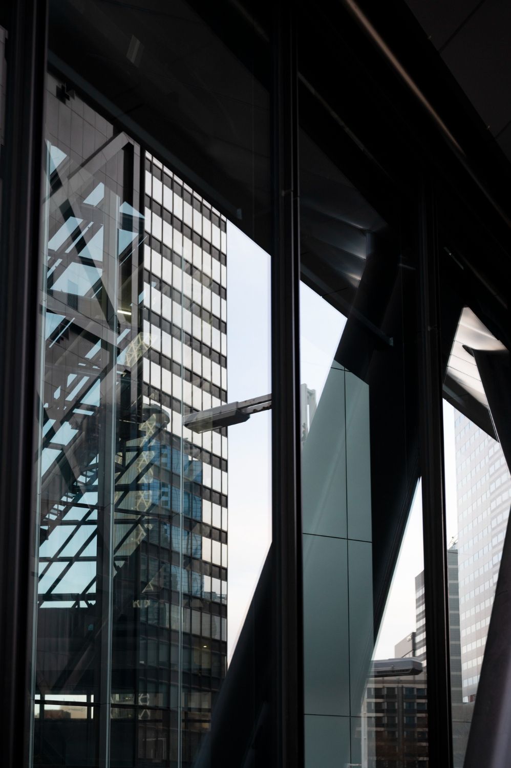 View of urban skyscrapers through a large, dark-framed geometric window with reflections.