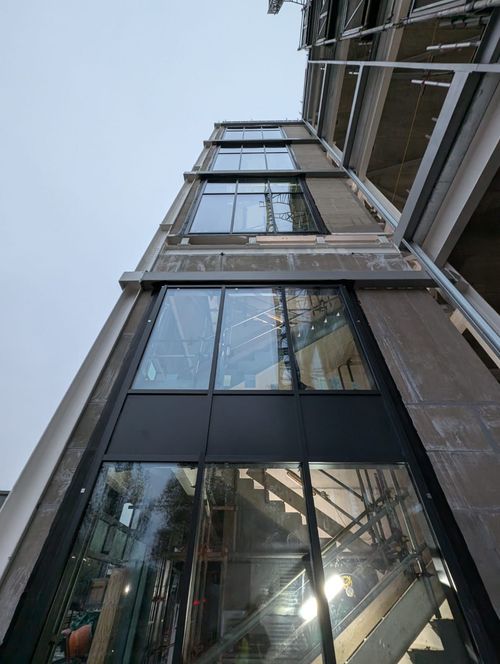 Modern glass office building exterior with a paved pedestrian plaza and patterned shadows in front.