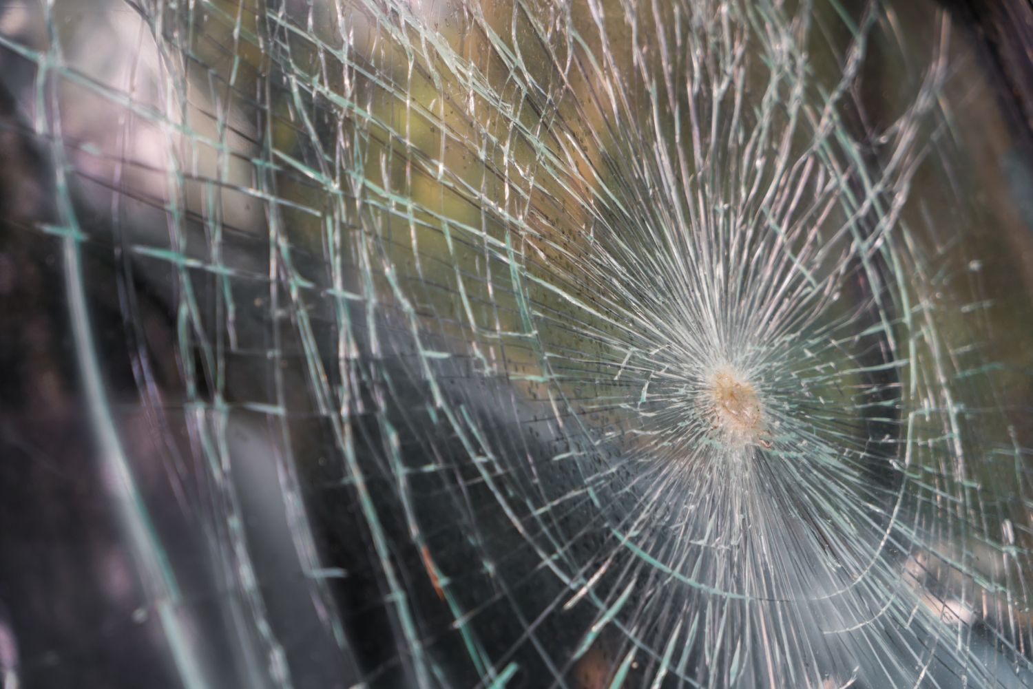 A close-up view of a car windshield with a circular impact point and a spiderweb pattern of cracks radiating outwards.