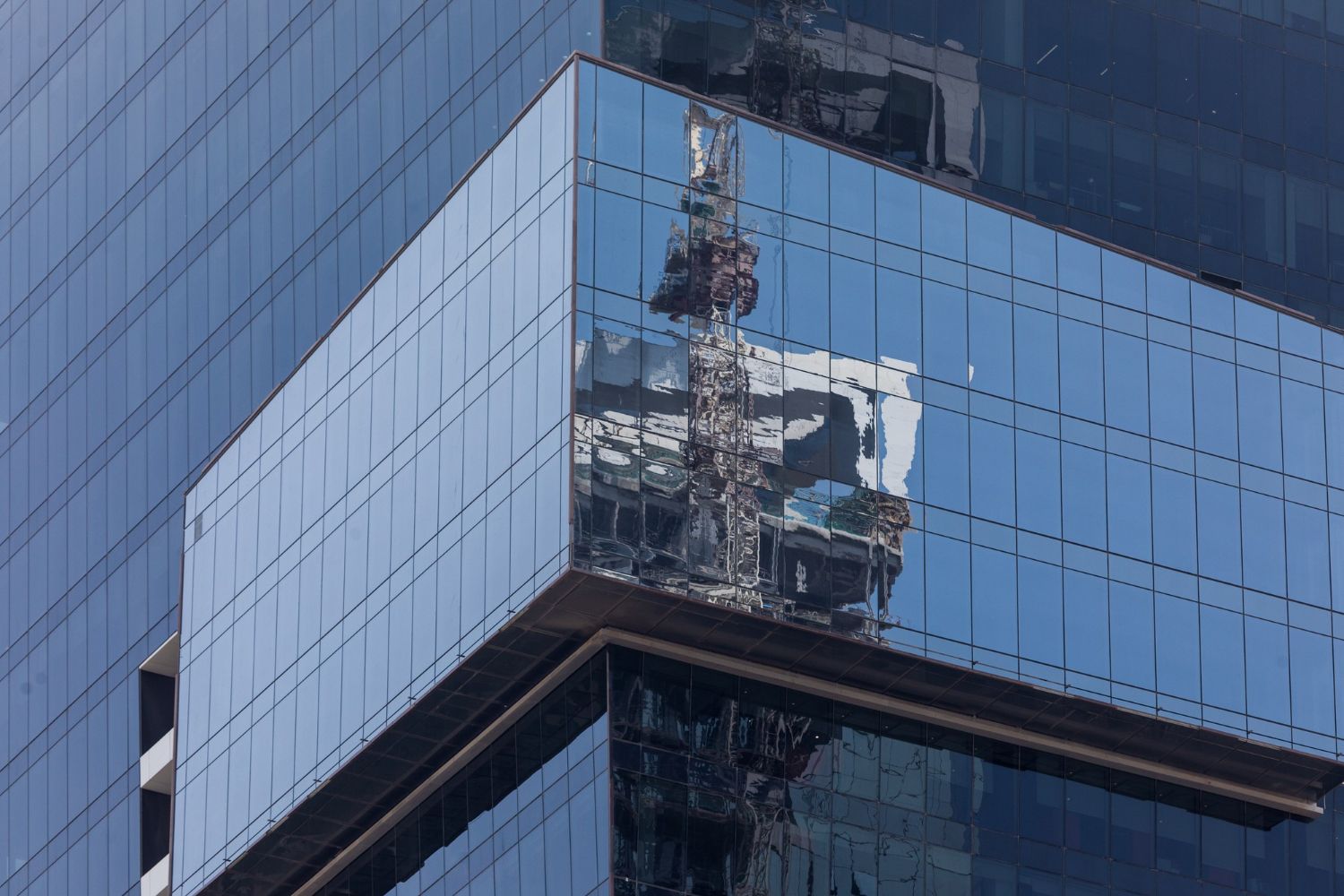 A high-rise glass building corner with a tower crane reflected in the mirrored windows.
