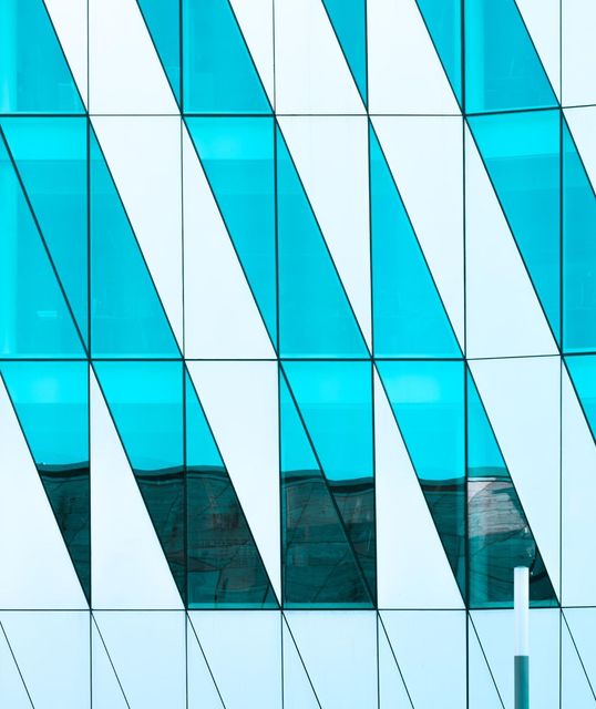 A modern building facade with alternating teal and white diagonal glass panels, creating a geometric pattern.