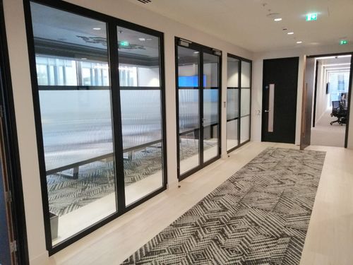 A bright, wide indoor corridor in a modern mall with glass-fronted storefronts and a glossy, speckled stone floor.