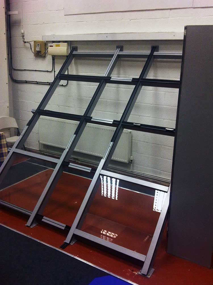 An empty, slanted black metal display rack mounted against a white brick wall in an indoor space.