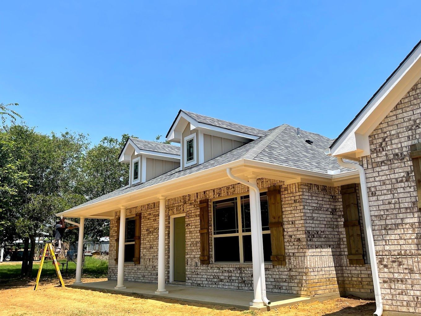 A brick house with a porch and a ladder in front of it.