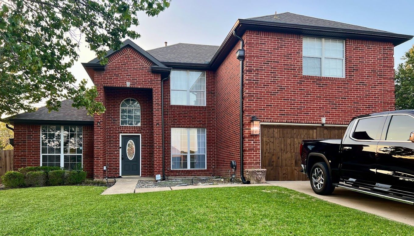 A black truck is parked in front of a large brick house.