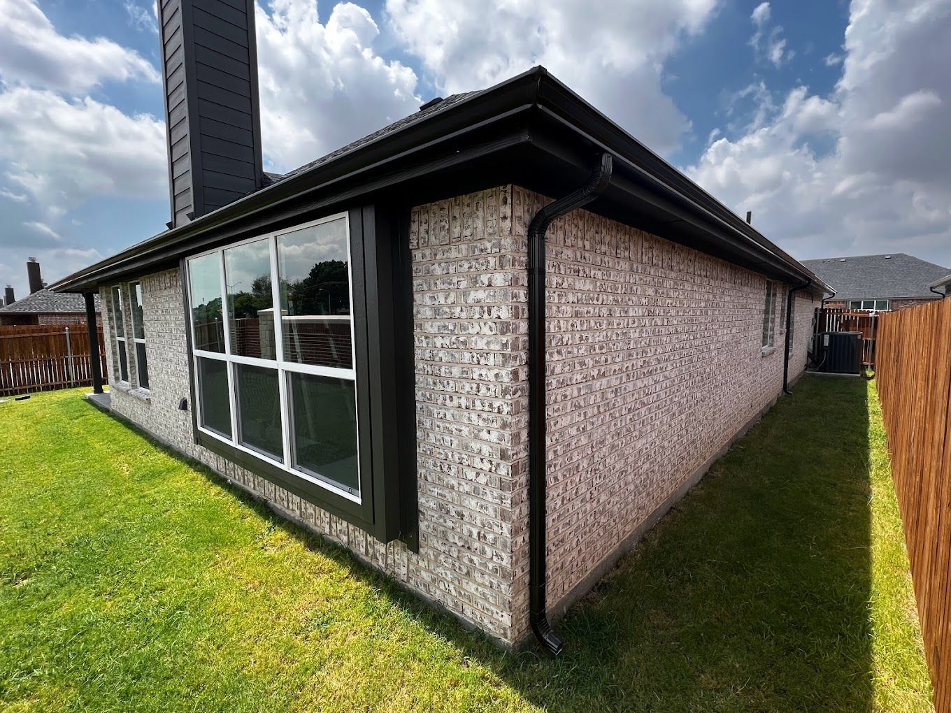The back of a brick house with a black gutter and a chimney.