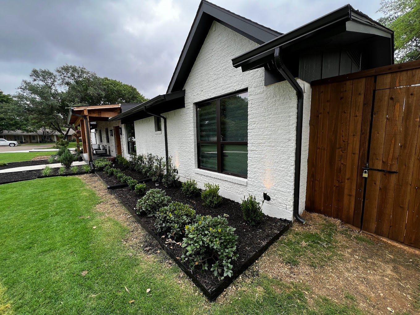 A white house with a black roof and a wooden fence in front of it.