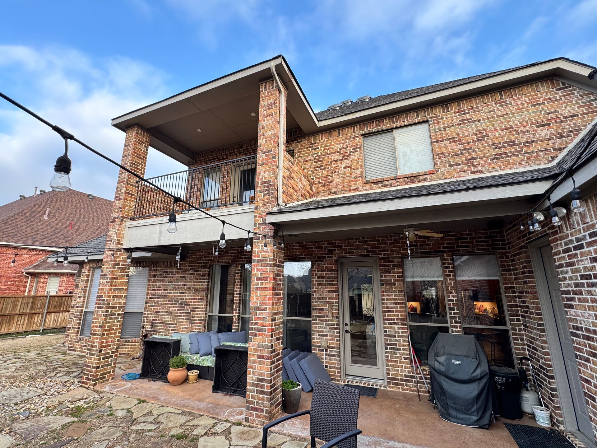 The backyard of a large brick house with a patio area and a grill.