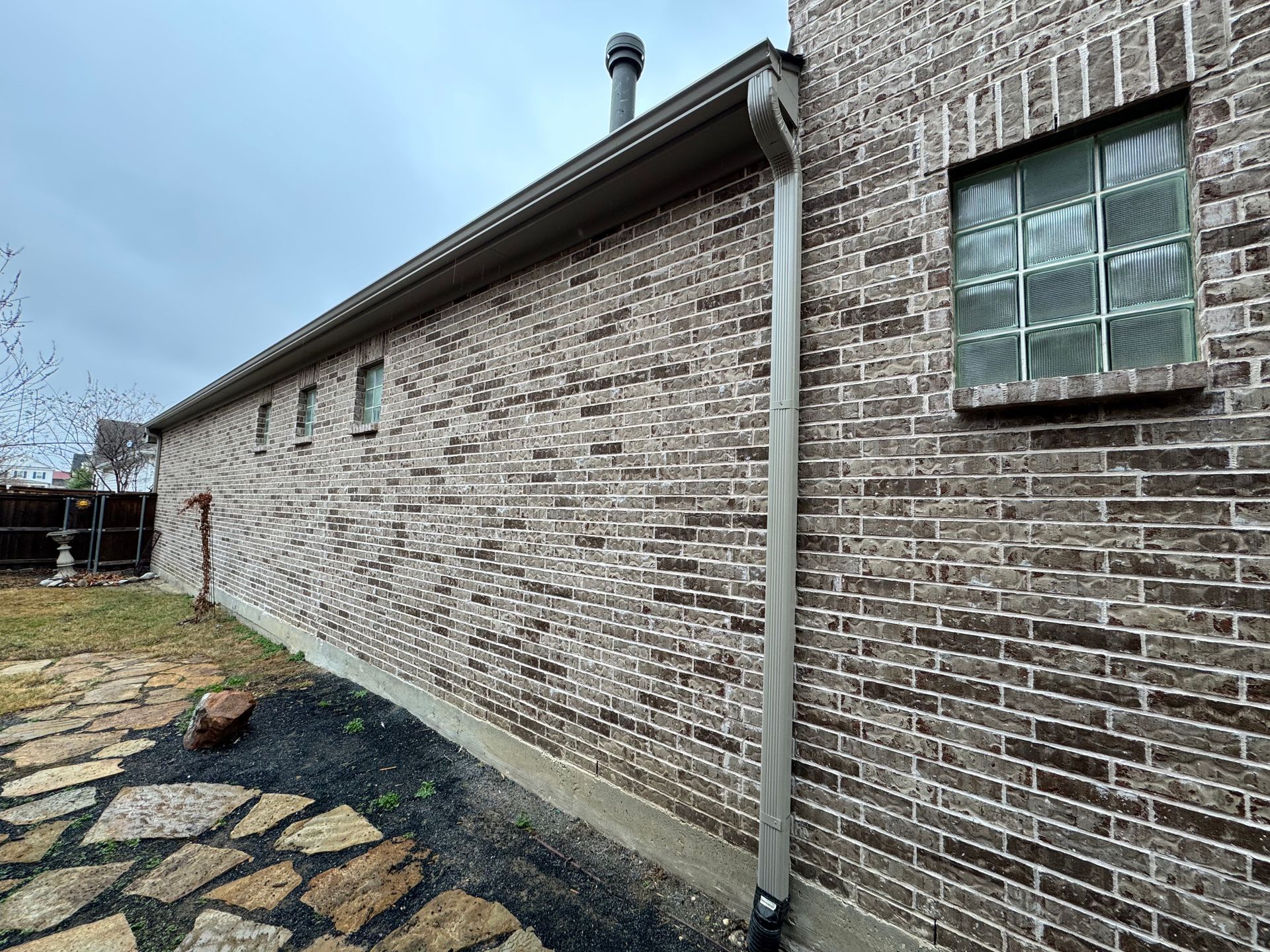 A brick house with a gutter on the side of it and a window.