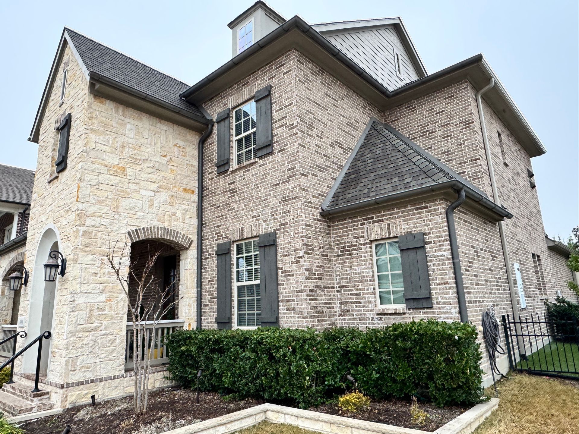 A large brick house with a gray roof and black shutters.