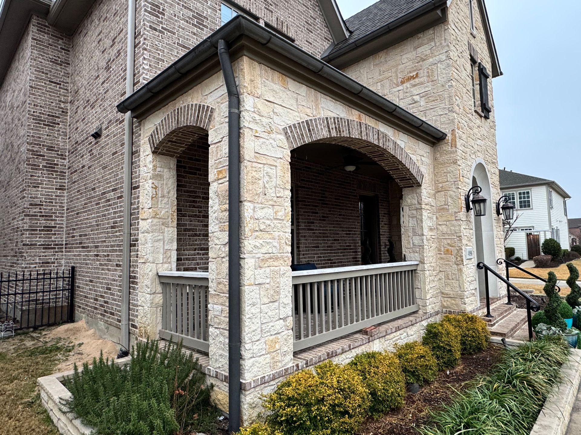 A brick house with a porch and a garden in front of it.