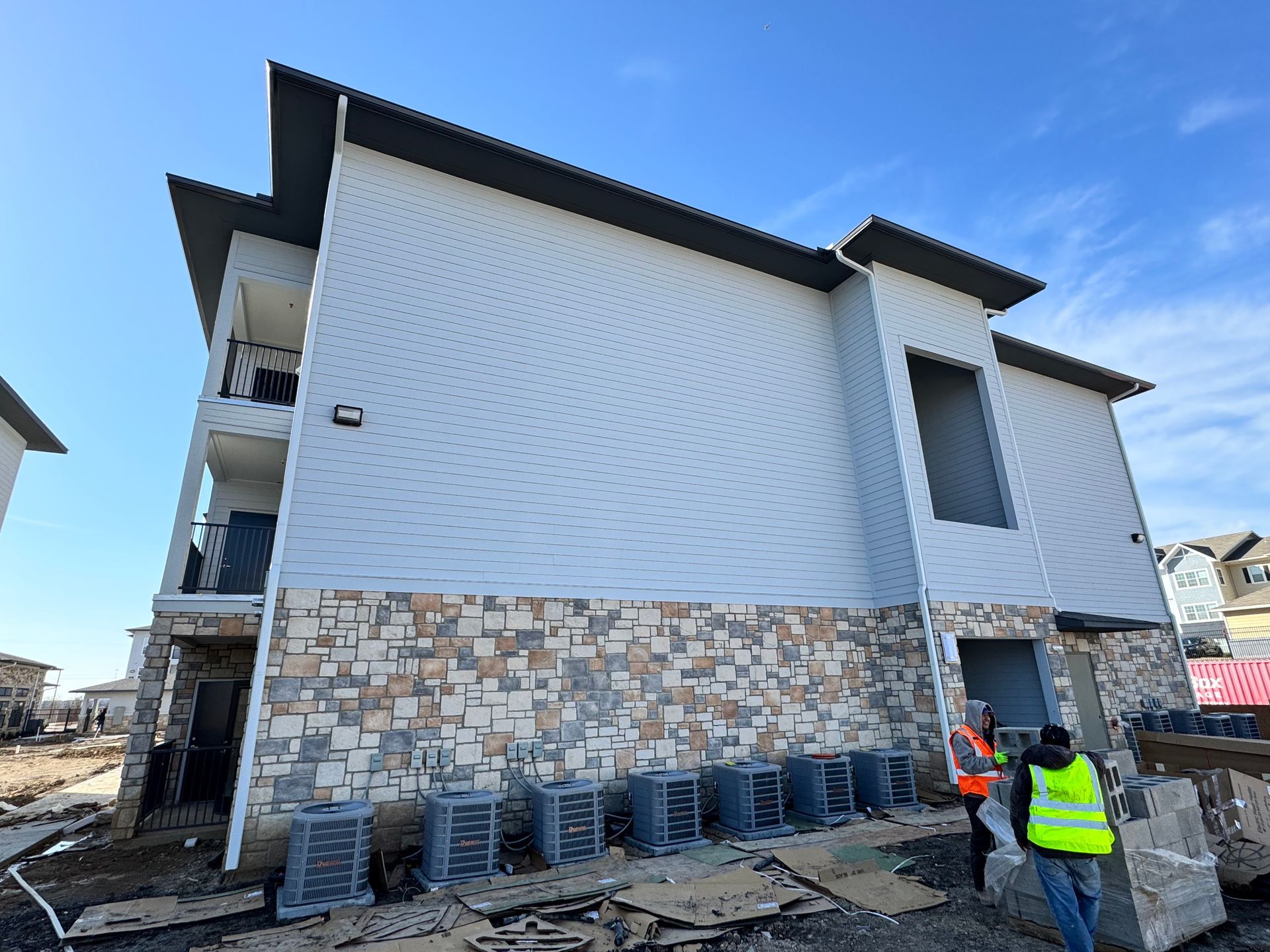 A man in a yellow vest is standing in front of a building under construction.