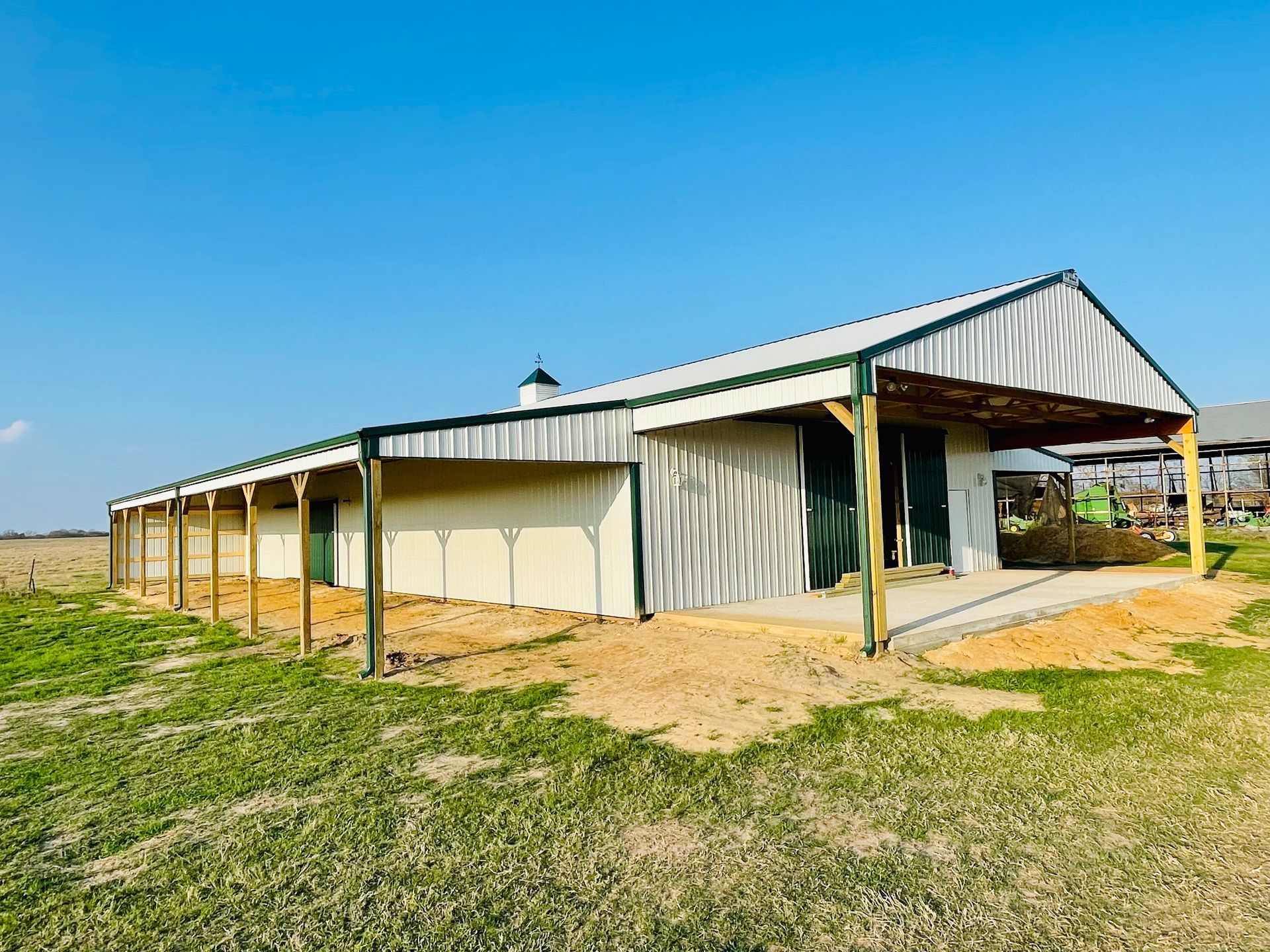 A large white building with a green roof is sitting in the middle of a grassy field.