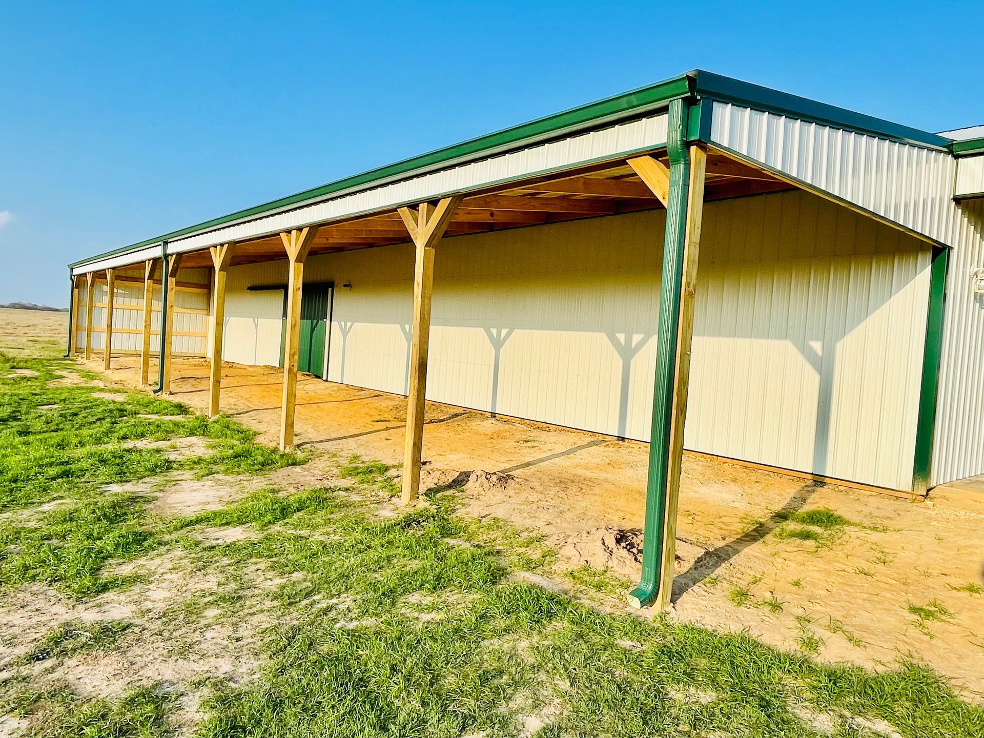 A large white building with a green roof is sitting in the middle of a field.