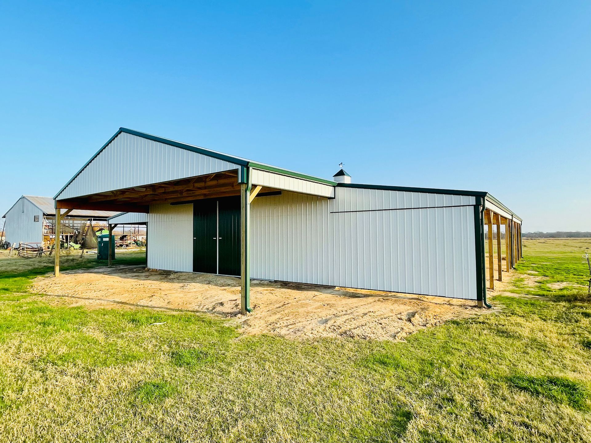 A white barn with a green roof is sitting in the middle of a grassy field.