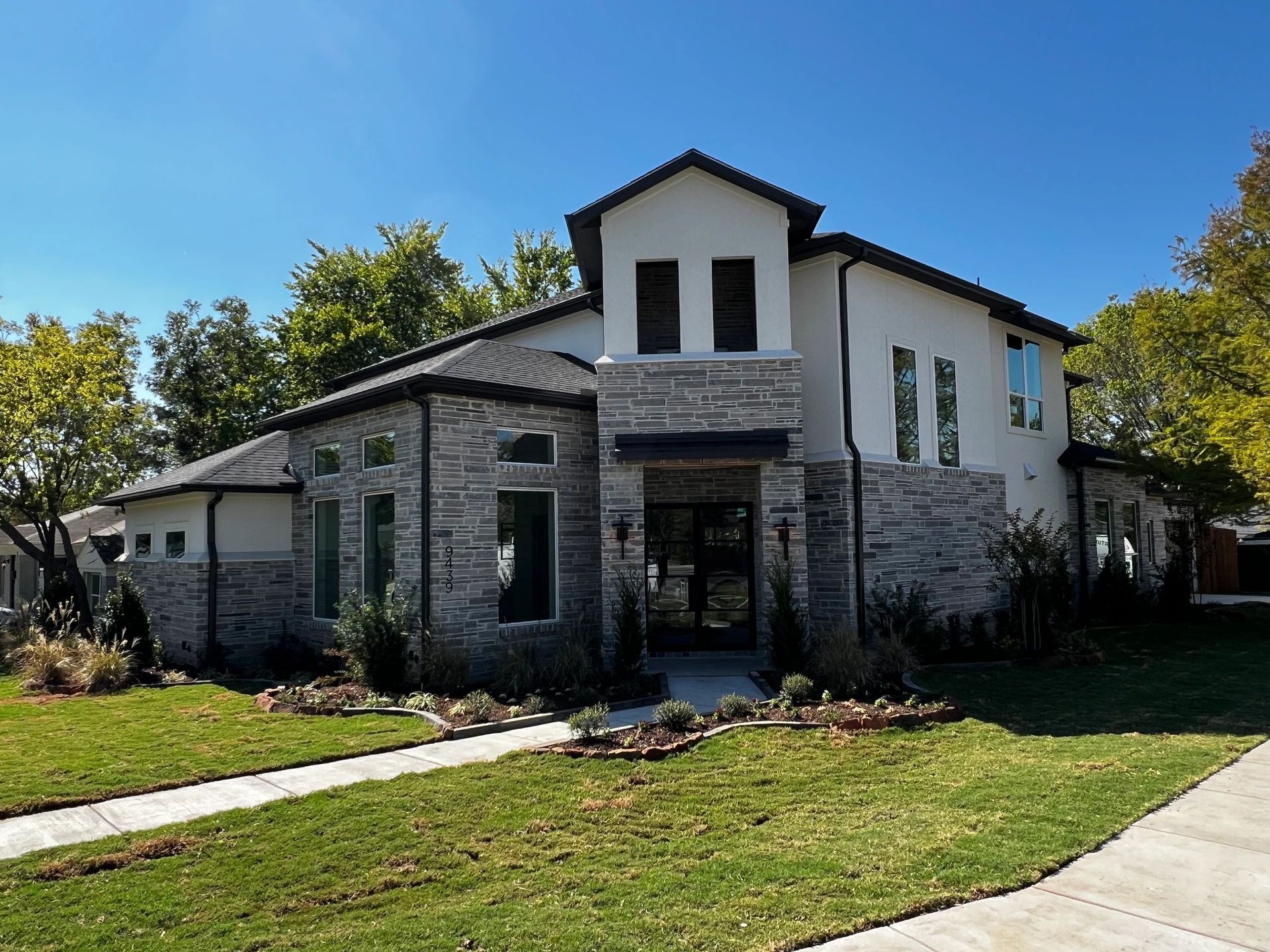 A large white and stone house with a lush green lawn in front of it.