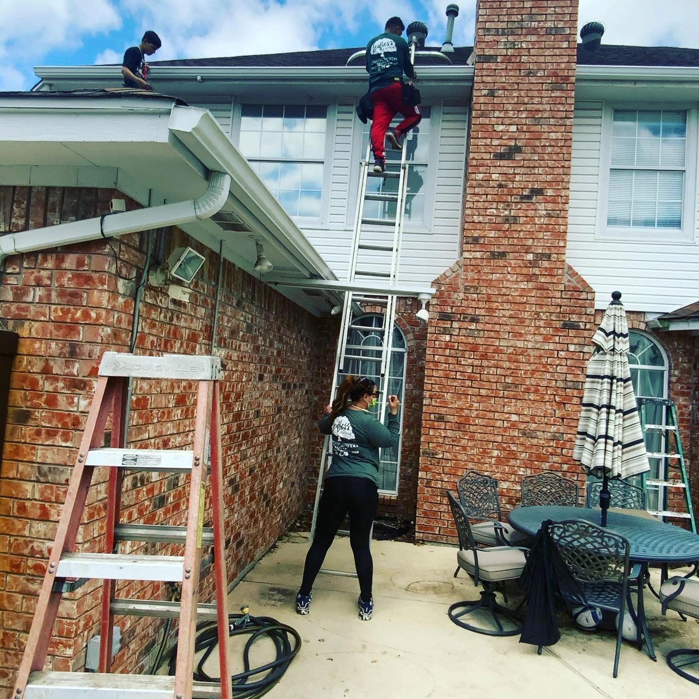 A woman is standing on a ladder in front of a brick house