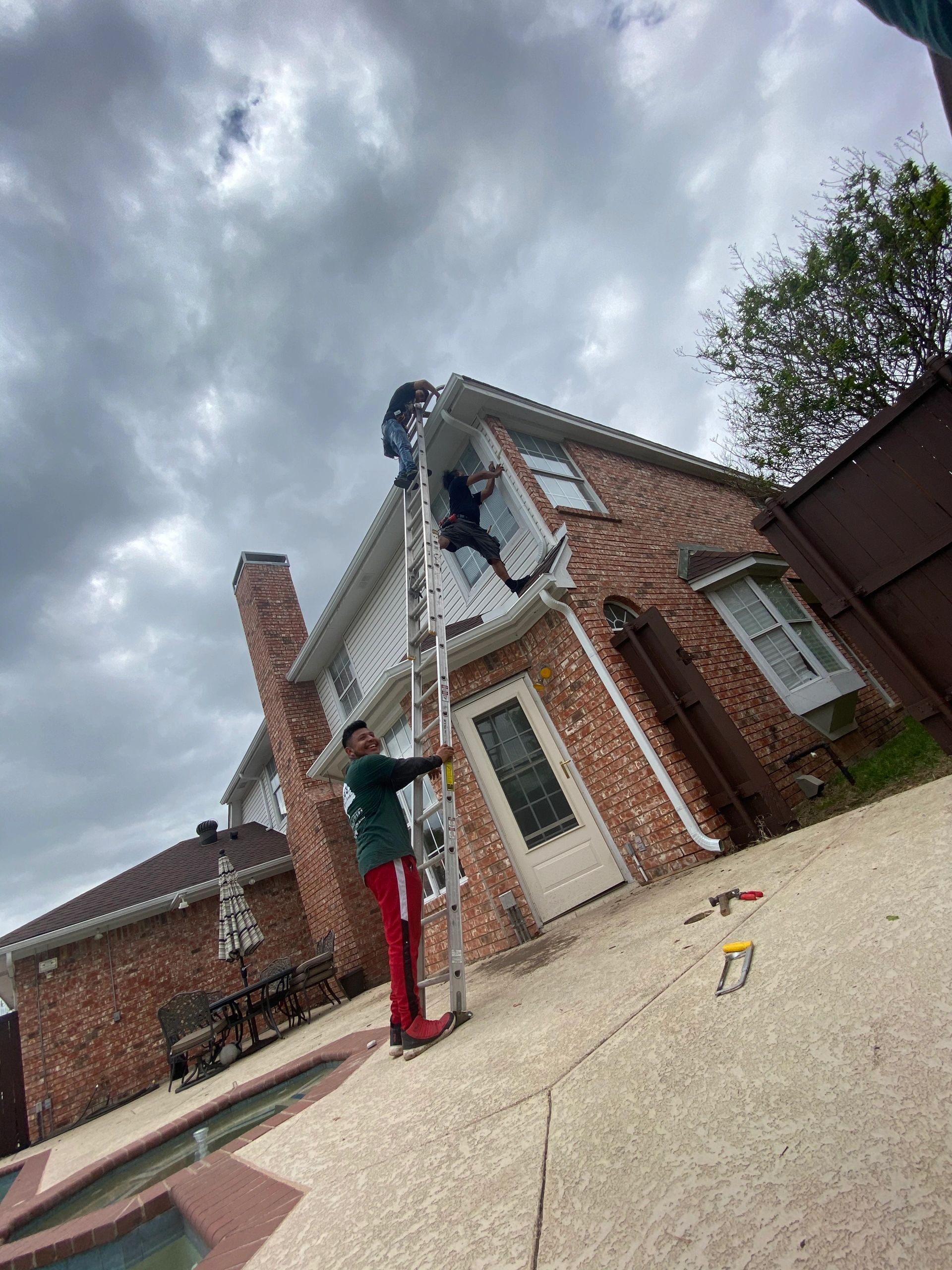 A man is standing on a ladder in front of a brick house.