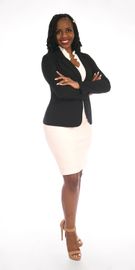 Woman in business attire, arms crossed, smiling. Black blazer, white top, beige skirt and heels, white background.