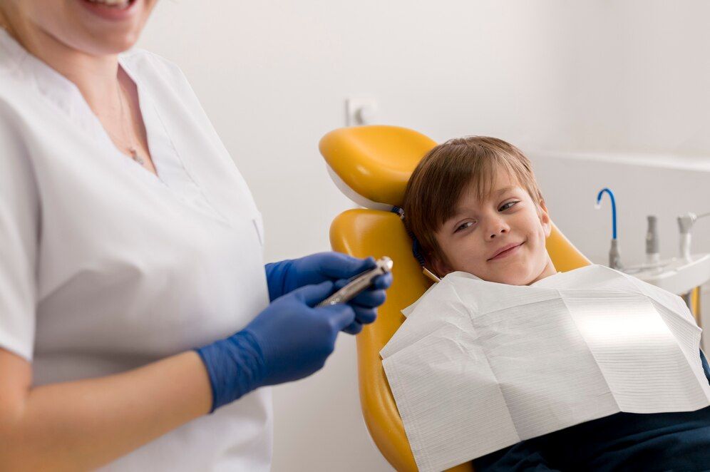 A young boy is sitting in a dental chair while a dentist holds a drill.