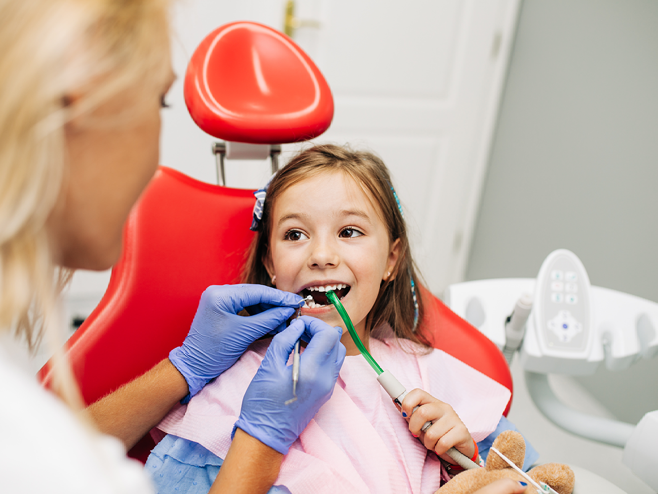 young girl in dental chair smiling while having her teeth looked at.