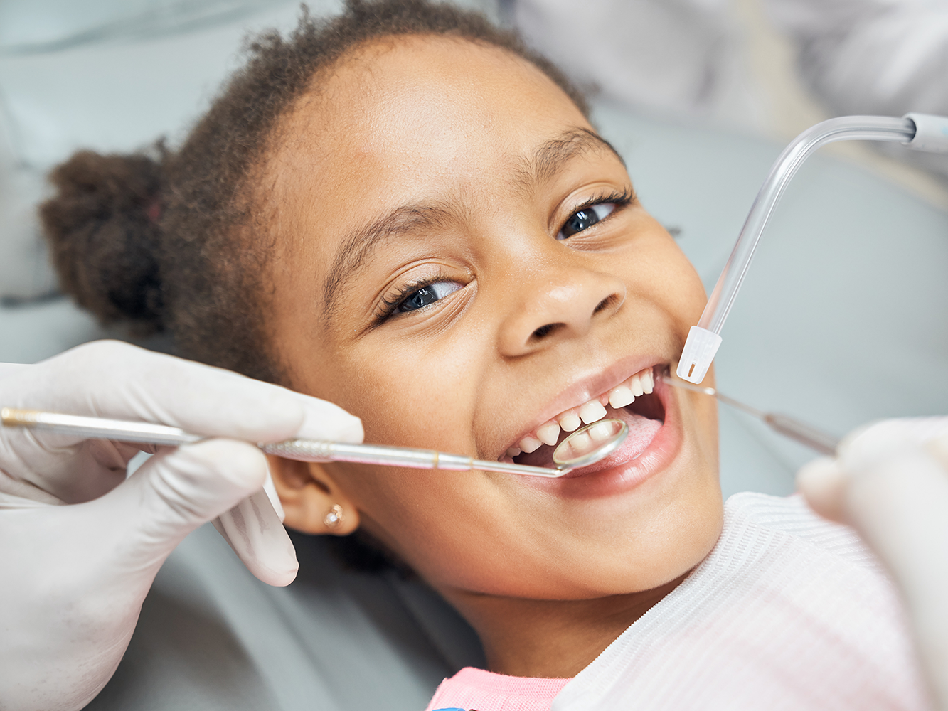 young girl sitting in dental chair smiling while doctor reviews her teeth