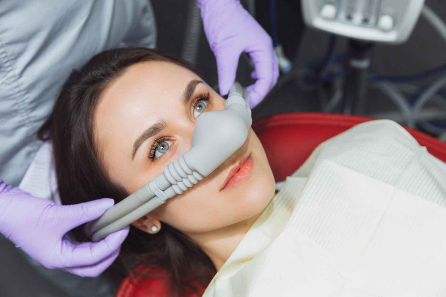 A woman is laying in a dental chair with an oxygen mask on her face.